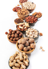 Assortment of nuts in bowls. Cashews, hazelnuts, walnuts, pistachios, pecans, pine nuts, peanuts, macadamia, almonds, brazil nuts. Food mix on white background, top view, copy space