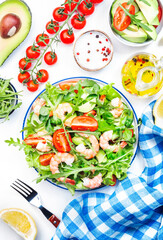 Fresh shrimp salad with tomatoes, lettuce, arugula, avocado, cucumber and lemon dressing on white background. Healthy eating, clean food concept. Top view