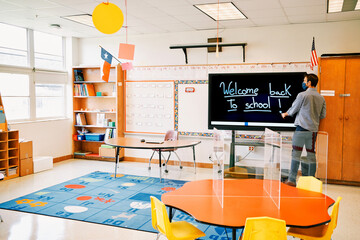 Elementary school teacher writing " Welcome back to school!" on a digital board, during Covid-19 pandemic.