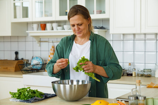 Middle aged woman adding lettuce to salad