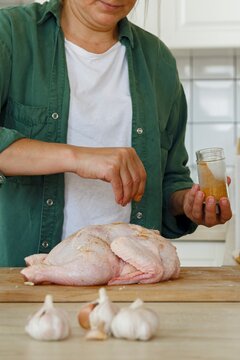 Crop woman adding spices to uncooked chicken