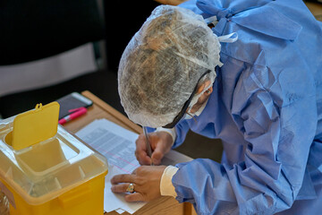 doctor in blue clothes checks vaccination list in front of plastic container