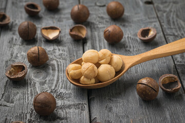 Wooden spoon with peeled macadamia nuts and unpeeled on a wooden table.