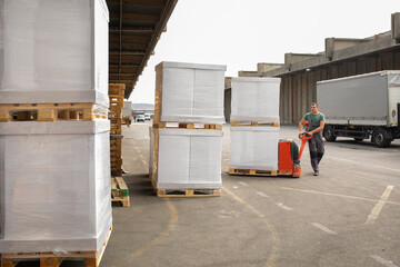 One man operates the pallet jack in front of a warehouse full of shipping goods