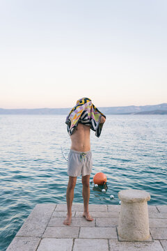 Unrecognizable shirtless young man standing on the dock and drying his head