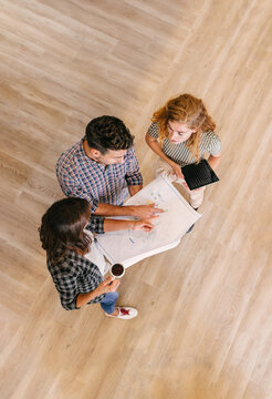 Shot from above of architects reviewing blueprints on a wooden floor