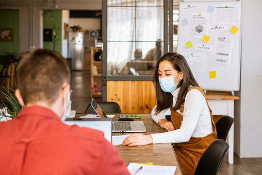 Confident female and man freelancer working together at office wearing protective face mask due to the coronavirus
