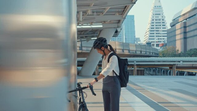 Smile  asian businesswoman with backpack use smart phone look camera in city stand at street with bike go to work at office. Sport girl use phone for work. Commute to work, Business commuter in city.