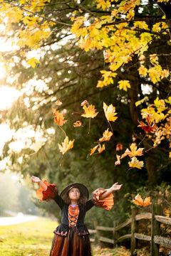 Girl in witch costume under falling leaves