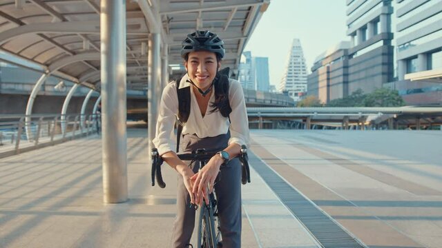 Asian businesswoman go to work at office stand and smiling wear backpack look at camera with bicycle on street around building on a city. Bike commuting, Commute on bike, Business commuter concept.