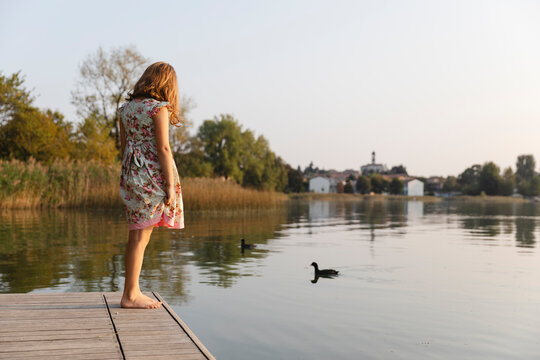 Little girl standing by the lake watching the ducks