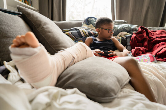 Boy on couch with leg in splint plays video games