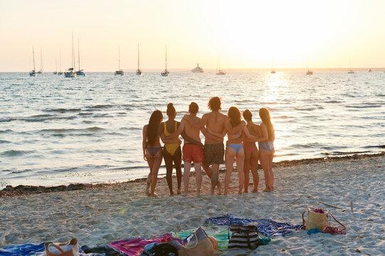 Friends standing on a beach watching a sunset