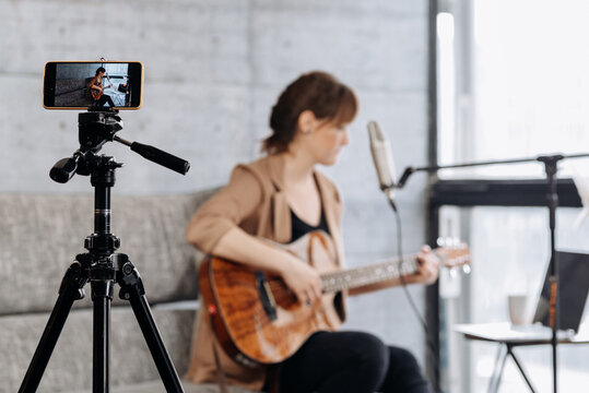 Woman recording video on smartphone and playing guitar