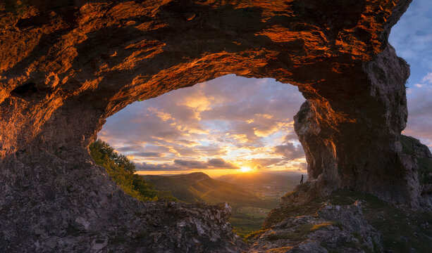 Woman watching sunset under a stone arch
