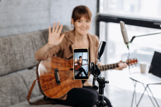 Smiling female guitarist recording video on smartphone at home