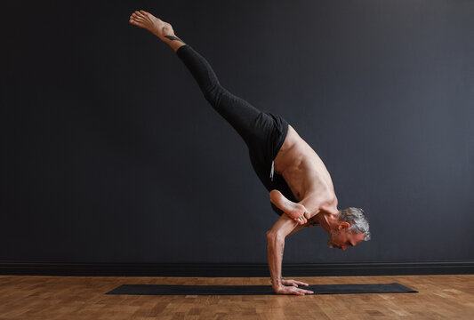 Slim middle aged male doing Eka Pada Kakasana pose