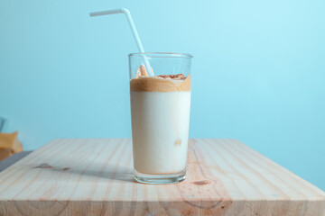 Homemade Dalgona coffee glass in a wooden textured tabletop. whisked instant coffee topping with fresh milk, making the delicious Korean drink. Trendy beverage with chocolate crumbs and white straw.