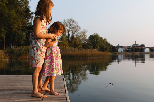 Little sisters look at the lake holding hands