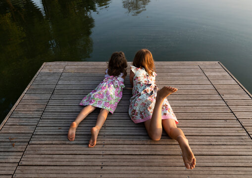 Little sisters lying together on the pier look at the lake