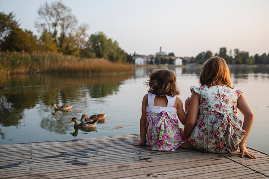 Little girls sitting by the lake watching the ducks