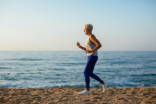 Middle aged jogger running near sea water at sundown