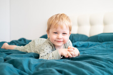 Little healthy toddler boy in green pajamas having fun lying in bed at home