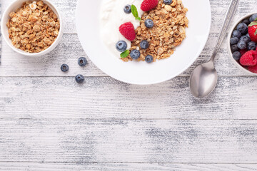 Yogurt with baked granola and berries in white ceramic plate on wooden background. Healthy breakfast. Copy space - Image