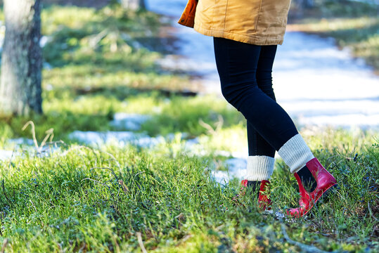 Autumn or spring concept with colorful forest and rain boots outside. Close up of woman feet walking in red boots.