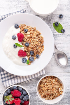 Homemade granola with yogurt and fresh berries in white ceramic plate on wooden background. Vertical photo - Image