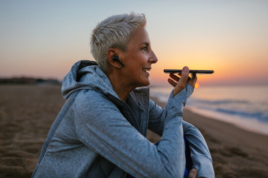 Happy mature athlete recording audio message near sea