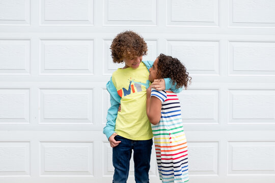 Multiracial brother and sister hug in front of garage