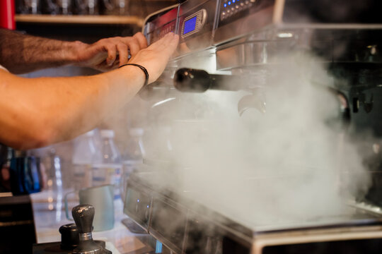 Detail of a professional coffe machine with barista hands and vapor in a cafeteria