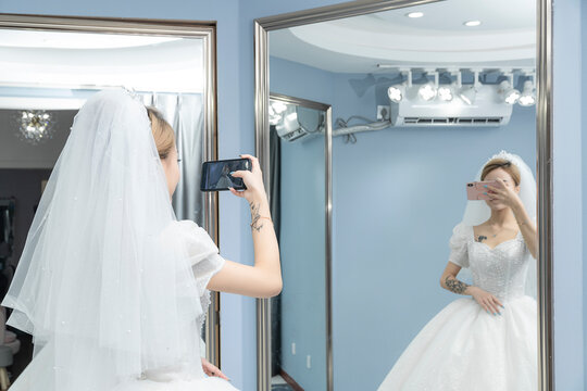 A woman in a wedding dress taking a picture of herself with her mobile phone