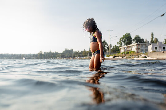 Curly haired girl in bikini wades into ocean