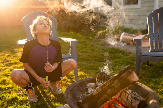 Boy crouched near campfire blowing on a smoking marshmallow