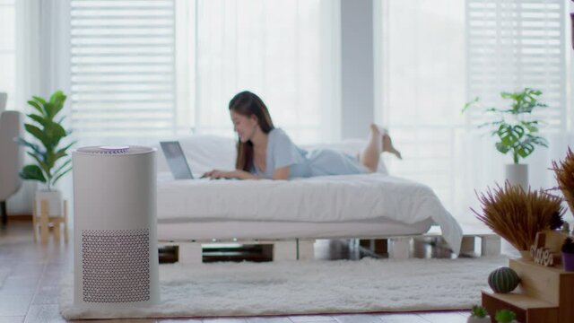 air purifier in bed room for clean dust and fresh air with woman working with computer laptop and relax in background