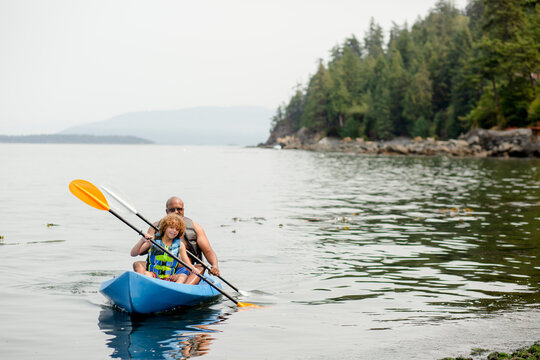 Black father and multiracial son kayak on ocean