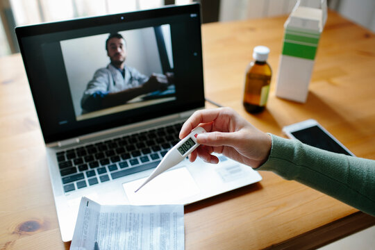 Woman's arms holding a thermometer while doing an online consultation with a doctor