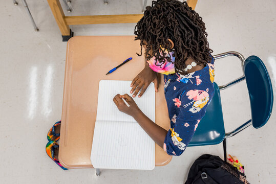 Black girl taking notes in a classroom during COVID-19
