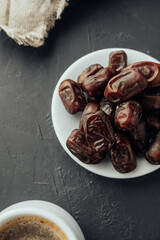 dried dates on farvor plate with coffee cup on dark background top view. traditional oriental sweets. healthy natural snack. vertical, selective focus