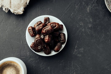 dried dates on farvor plate with coffee cup on dark background top view. traditional oriental sweets. healthy natural snack. selective focus
