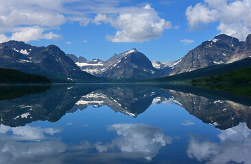 the reflection of  mountain peaks in glacier park national park, montana, in the mirrorlike surface of lake sherburne im the many glacier valley along the road to many glacier in the summer