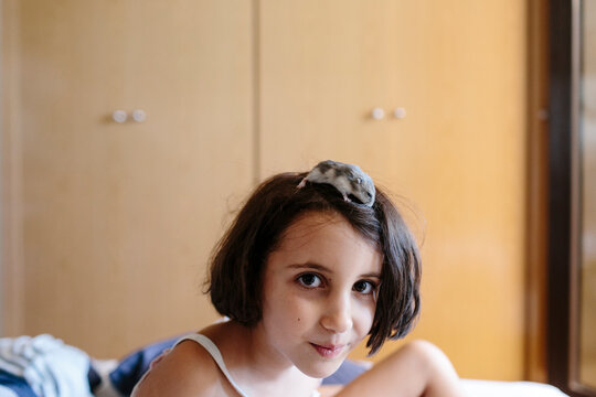 Kid with hamster on her head looking at camera.