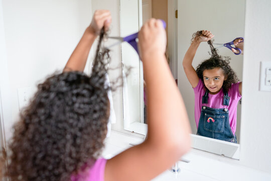 Girl looking in mirror prepares to cut hair with scissors
