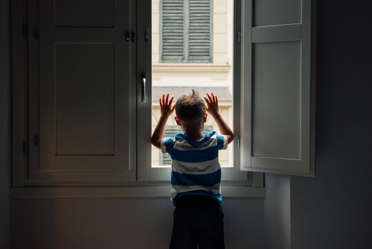 Little boy stuck indoors and looking out his second floor window.