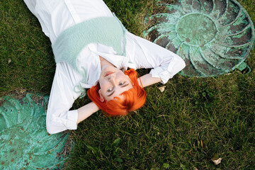 charming smiling red-haired woman lying on the grass