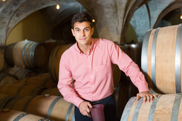 Fototapeta na wymiar Happy male owner of winery standing with wine in cellar