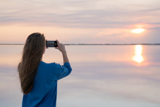 Female taking a photo of sunset on lake background