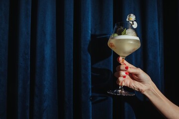 Hand holding cocktail against blue curtain